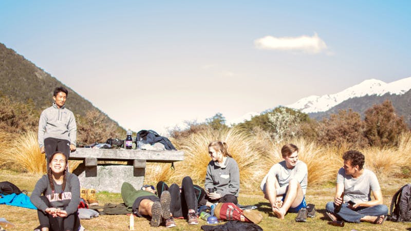 A group of students takes a break while on a hiking trip in New Zealand mountains.