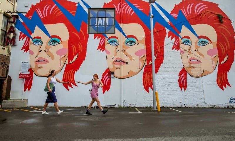 People having fun in front of a big wall of graffiti of three identical faces with red hair